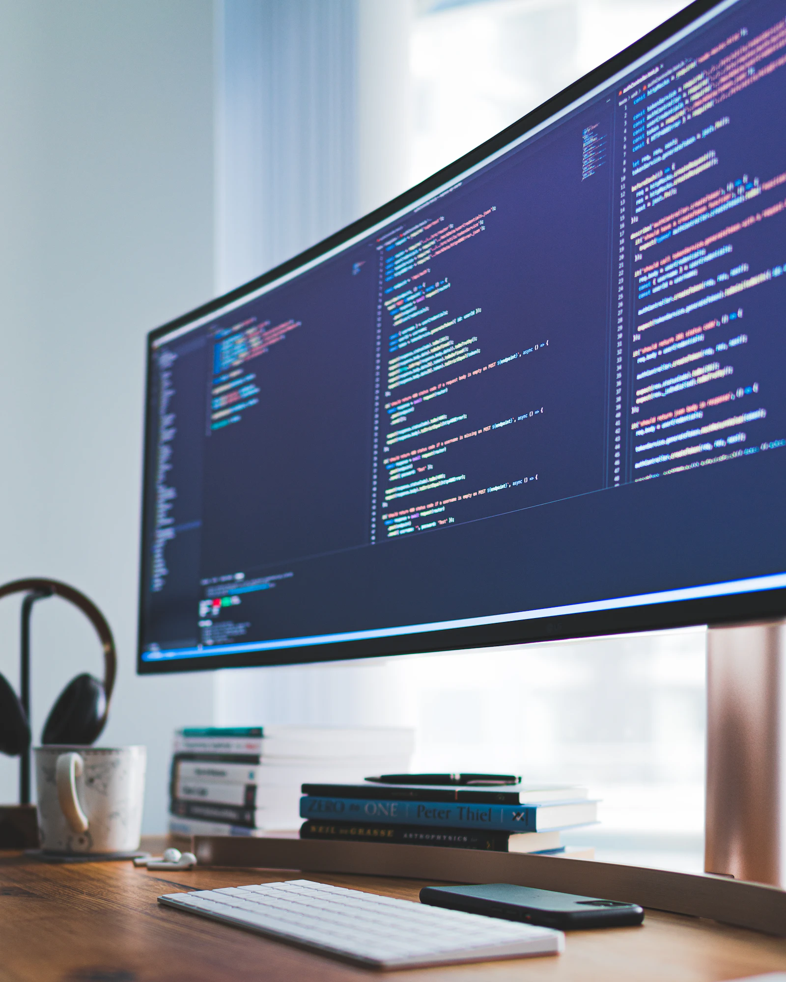 A developer's desk with code displayed on a wide monitor